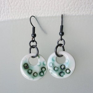 Boucles d&#39;oreilles en porcelaine blanche avec le modèle aléatoire noir et vert de cercle sur les crochets noirs antiques de boucle d&#39;oreille