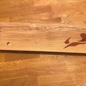 Op de afbeelding: Een houten snijplank met een decoratief ontwerp van een gestileerde vlam in roodbruine kleur. De plank heeft een natuurlijke houtnerf en een lichtbruine kleur.