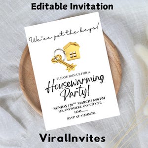 Pode incluir: Um cartão de convite branco com o texto "Editable Invitation" no topo. O cartão apresenta uma chave de casa dourada e um pingente de casa, com as palavras "We've got the keys!" e "Housewarming Party!" impressas. O convite inclui detalhes do evento e informações de RSVP.