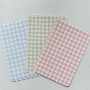 Puede incluir: Tres tarjetas rectangulares con esquinas redondeadas, cada una con un patr&oacute;n de cuadros vichy. Las tarjetas son de colores pastel: azul claro, verde p&aacute;lido y rosa. El patr&oacute;n de cuadros vichy consiste en peque&ntilde;os cuadrados espaciados uniformemente.