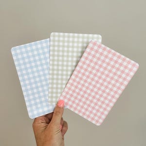 Puede incluir: Tres tarjetas rectangulares con un patr&oacute;n de cuadros vichy en colores pastel: azul, verde y rosa. Las tarjetas se sostienen en una mano sobre un fondo neutro. El patr&oacute;n de cuadros vichy es un dise&ntilde;o cl&aacute;sico de cuadros peque&ntilde;os.