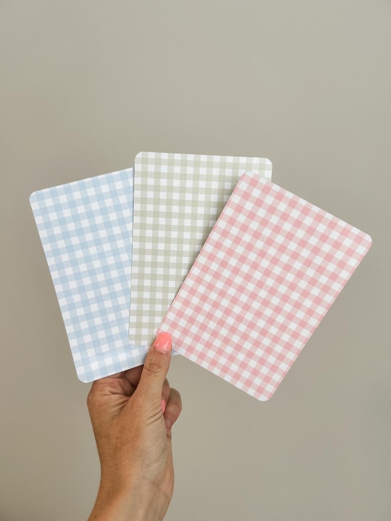 Puede incluir: Tres tarjetas rectangulares con un patr&oacute;n de cuadros vichy en colores pastel: azul, verde y rosa. Las tarjetas se sostienen en una mano sobre un fondo neutro. El patr&oacute;n de cuadros vichy es un dise&ntilde;o cl&aacute;sico de cuadros peque&ntilde;os.