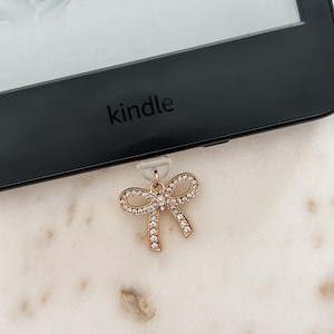 May include: A gold bow bookmark with clear rhinestones attached to a Kindle e-reader.