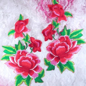 May include: Two red and pink embroidered flower appliques with green leaves. The flowers have a layered design with pink and red stitching.