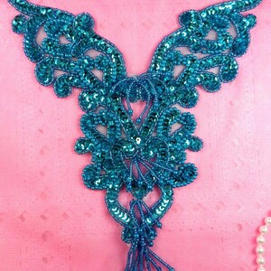 May include: A teal blue sequined and beaded applique with a floral design and a tassel. The applique is perfect for adding a touch of sparkle to clothing or crafts.
