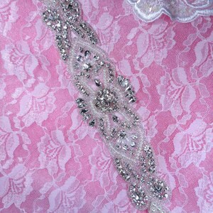 Peut inclure: Une délicate embellissement perlée avec un design argenté et blanc. L'embellissement est fait de petites perles rondes et de strass, disposés en un motif floral. Il est parfait pour ajouter une touche d'éclat à tout projet.