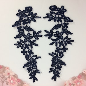 May include: Two black lace appliques with a floral design. The appliques are shaped like a teardrop and have a delicate, intricate pattern.