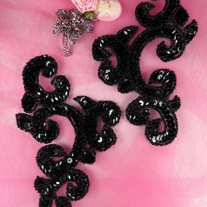 May include: Two black sequined embellishments in a floral design on a pink background.