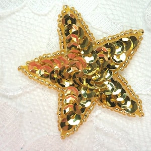 May include: A gold star-shaped embellishment made of sequins and beads. The star is about 2 inches wide and 2 inches tall.