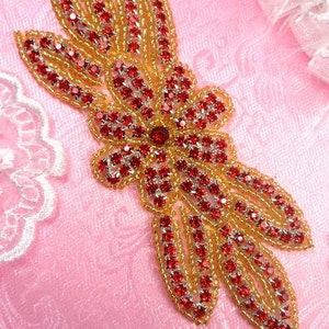 May include: A red and gold beaded applique with a floral design. The applique is made of small, round beads that are sewn together to create a delicate and intricate pattern.