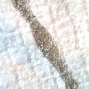 May include: A silver rhinestone trim with a floral design. The trim is made of small, clear rhinestones that are arranged in a repeating pattern of flowers.