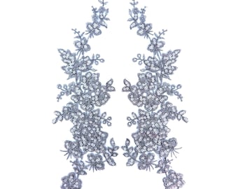 May include: Two silver sequined floral appliques with a delicate lace design. These appliques are perfect for adding a touch of sparkle and elegance to any project.