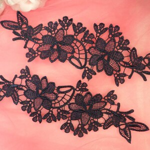 May include: Two black lace appliques with floral designs. The appliques are delicate and intricate, with a variety of flower shapes and sizes.