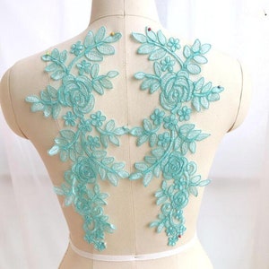 May include: Two turquoise lace appliques with floral designs, featuring delicate leaves and roses. The appliques are perfect for adding a touch of elegance to clothing, crafts, or home decor.