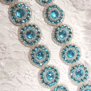 May include: Two rows of turquoise blue and silver beaded embellishments with a large, round, turquoise blue rhinestone in the center of each embellishment.
