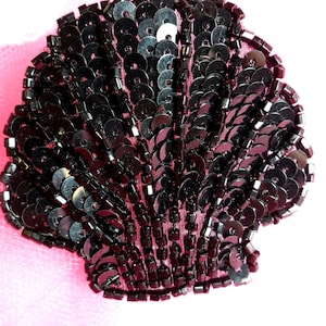 May include: Black sequined seashell applique. The shell is made of black sequins sewn onto a fabric base.