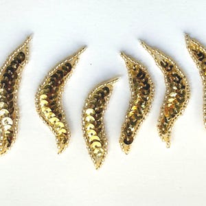 May include: Six gold sequined leaf-shaped embellishments. Each embellishment is about 2 inches long and has a curved shape.