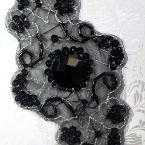 Peut inclure: Embellissement noir en sequins et perles sur un tissu noir transparent. L'embellissement présente un grand strass noir au centre.