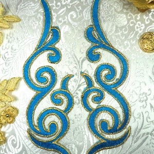 May include: Two blue and gold embroidered fabric appliques with a swirling design. The appliques are on a white background.