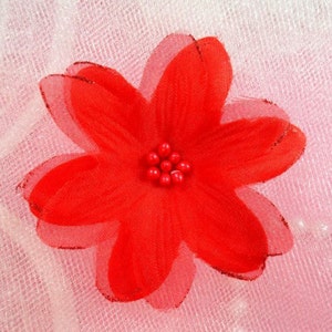 May include: A red fabric flower with a center of red beads. The flower is on a white and pink background.
