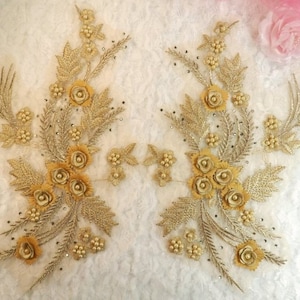 Peut inclure: Deux appliques florales dorées avec des accents perlés. Chaque applique présente un groupe de cinq fleurs dorées avec un motif feuillu.