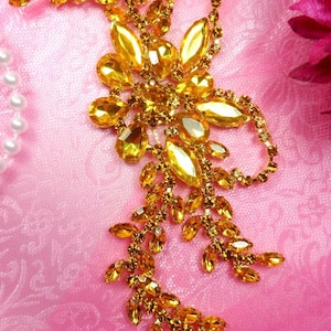 May include: A gold-toned rhinestone embellishment with a floral design. The embellishment is made of small, faceted rhinestones that are arranged in a delicate pattern. It is perfect for adding a touch of sparkle to any project.