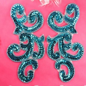 May include: Two turquoise blue sequined fabric appliques in a swirling, floral design. The appliques are on a pink background.
