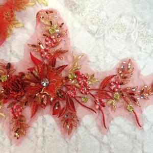 Peut inclure: Applique florale rouge et dorée avec des paillettes et des perles. L'applique est sur un fond de tissu transparent.