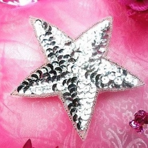 May include: A silver star-shaped patch made of sequins on a pink background.