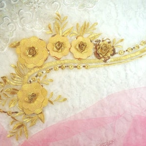 Peut inclure: Applique florale brodée en or avec des paillettes et des perles. L'applique présente un groupe de cinq fleurs avec des feuilles et des tiges.