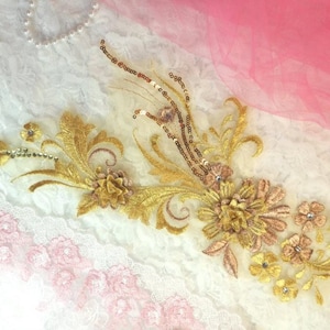 Peut inclure: Broderie florale dorée et brune avec des paillettes sur un tissu en dentelle blanche.