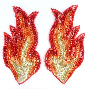 May include: Two flame-shaped appliques. Each applique is made of red, orange, and gold sequins and beads, creating a fiery effect. The appliques are set against a white background.