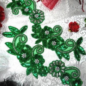 May include: Two green floral appliques with silver sequins and beads. The appliques are on a white background.