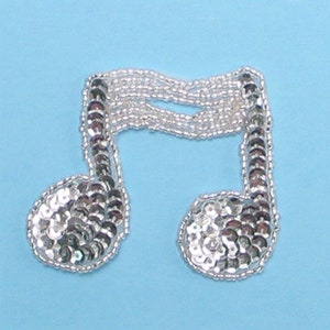 May include: A silver musical note made of sequins and beads. The note is a common symbol for music and is often used in crafts and decorations.