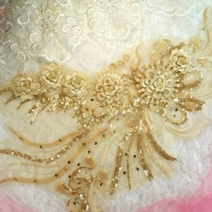 Peut inclure: Applique florale dorée et ivoire avec des paillettes et des perles. L'applique est sur un fond de dentelle blanche.