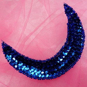 Può includere: Un ornamento a forma di mezzaluna blu fatto di paillettes su uno sfondo di tulle rosa.