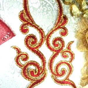 Puede incluir: Dos adornos de tela bordados en oro y rojo con un diseño floral en espiral.