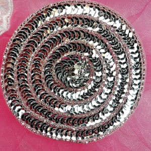 May include: A silver circular embellishment made of small, round sequins arranged in a spiral pattern.