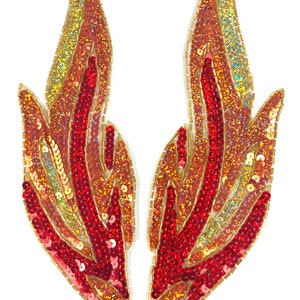 Pode incluir: Duas aplicações em forma de chama, adornadas com lantejoulas. A combinação de cores varia do vermelho ao dourado. As bordas são contornadas com contas douradas. Estas aplicações decorativas podem ser usadas para embelezar roupas ou acessórios. Cada aplicação tem cerca de 15 cm de comprimento.