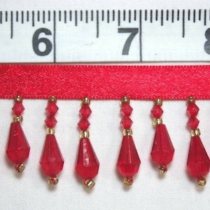 Pode incluir: Franja de contas vermelhas com suporte de fita de cetim. A franja é feita de pequenas contas vermelhas em forma de lágrima com detalhes dourados.