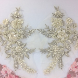 Może przedstawiać: Dwa delikatne kwiatowe aplikacje z koralikami i haftem srebrnym i białym. Aplikacje są na przezroczystej białej tkaninie i mają kwiatowy wzór z liśćmi i kwiatami.