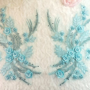 Peut inclure: Deux appliques florales bleu clair avec des accents de perles. Chaque applique présente un groupe de fleurs en satin et des feuilles délicates.