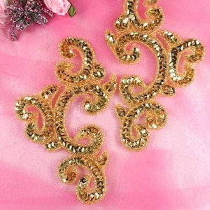 May include: Two gold sequined fabric appliques in a swirling, ornate design. The appliques are perfect for adding a touch of sparkle to clothing, bags, or home decor projects.