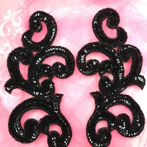 May include: Two black sequined fabric appliques in a floral design. The appliques are on a pink background.
