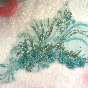 Peut inclure: Applique florale bleu turquoise avec des paillettes et des perles sur un fond de tissu transparent.