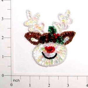 May include: A sequined Christmas reindeer head with a red nose, black smile, and brown antlers. The reindeer is decorated with iridescent sequins and a sprig of holly. The image is on a white background.