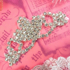 May include: A silver rhinestone embellishment in the shape of a heart with a pink background.