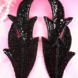 Peut inclure: Deux appliques en tissu noir à paillettes en forme de flammes stylisées. Les appliques sont faites de paillettes et de perles noires.