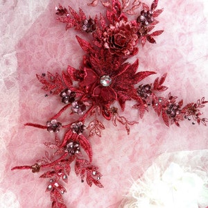 May include: Burgundy red floral applique with a rhinestone center. The applique is made of lace and has a delicate, intricate design.