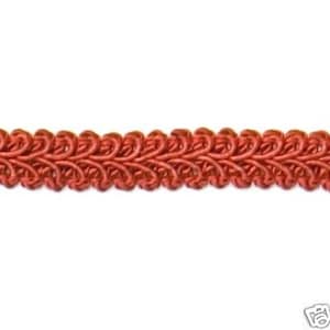 May include: A length of coral-colored gimp braid trim. The trim features a repeating pattern of looped knots, creating a textured, decorative edge. The braid is against a white background.